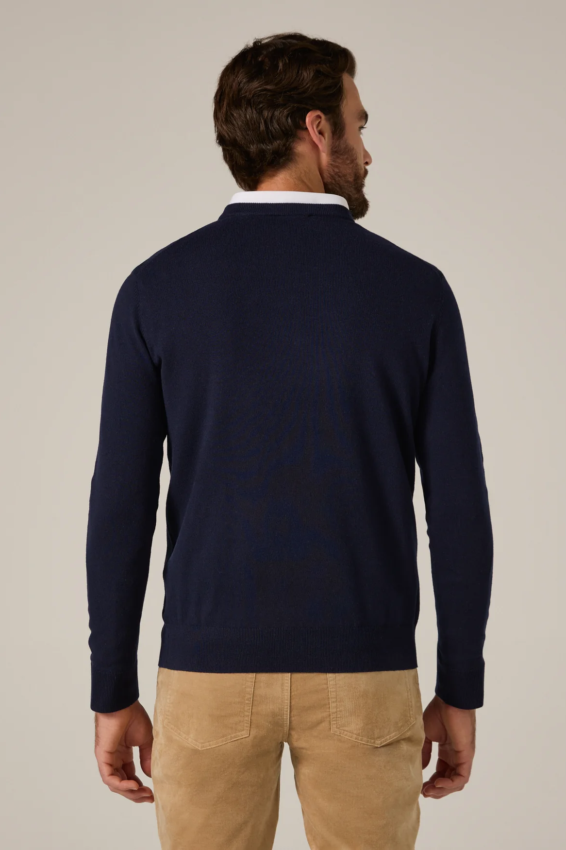 Man wearing a navy sweater and beige pants against a plain background