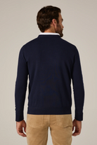 Man wearing a navy sweater and beige pants against a plain background