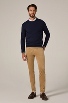 Man wearing a navy sweater, white shirt, beige pants, and brown shoes on a plain background