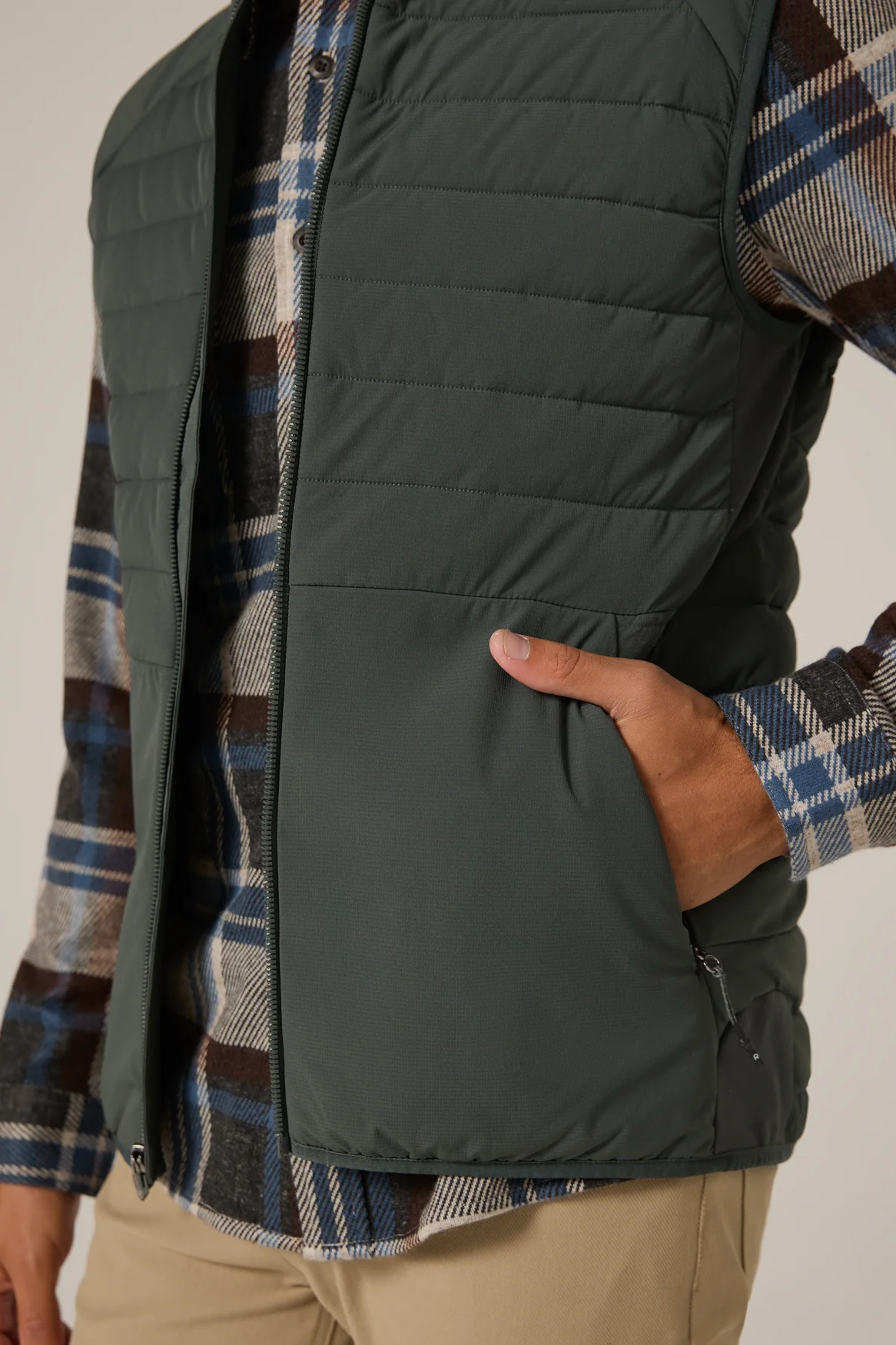 Person wearing a dark green puffer vest over a plaid shirt with a neutral background