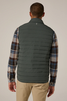 Man wearing a green puffer vest over a plaid shirt with a beige background