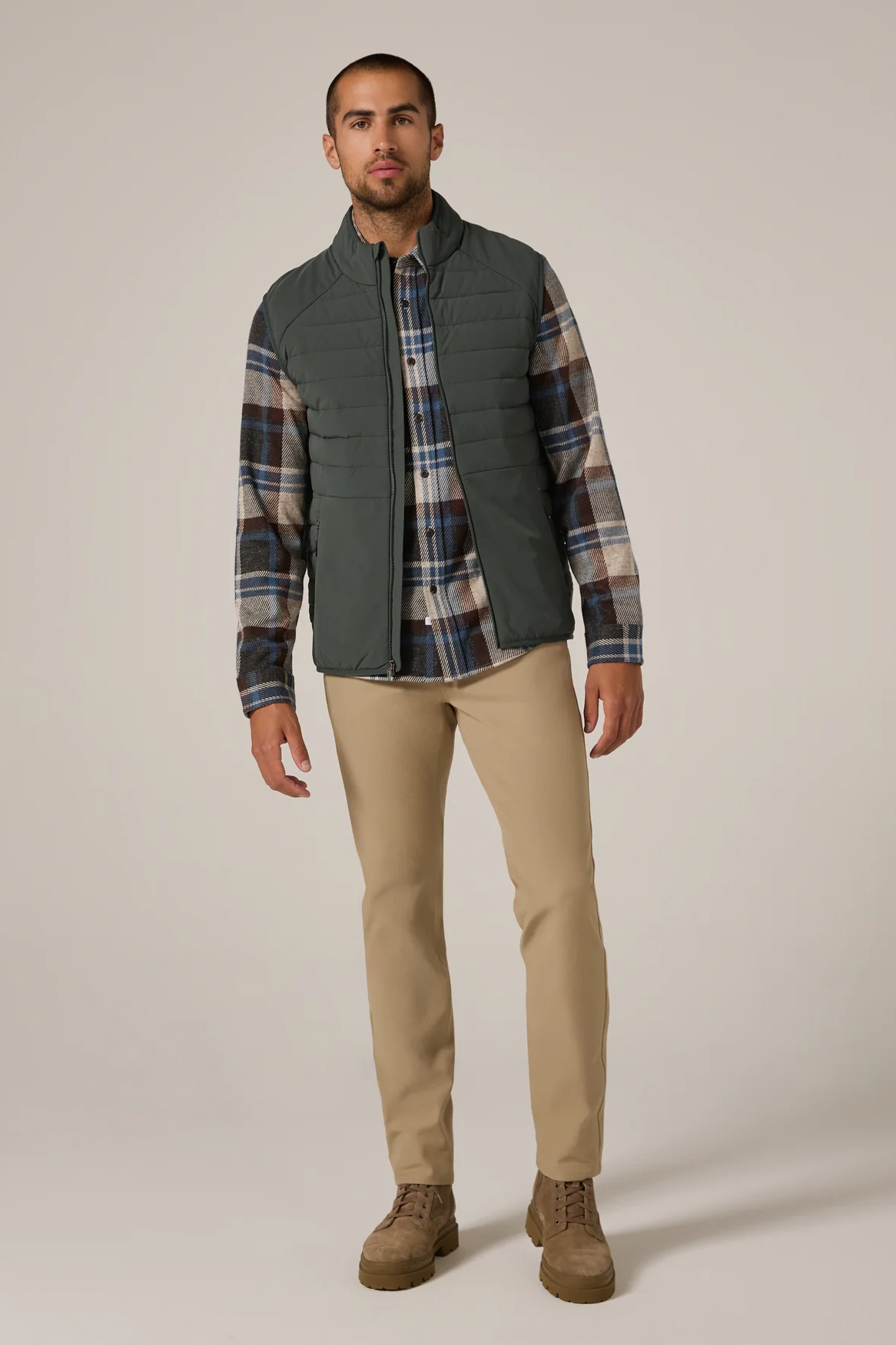 Man wearing a plaid shirt, vest, and pants on a plain background