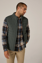 Man wearing a plaid shirt and green vest against a neutral background