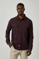 Man wearing a dark brown button-up shirt with beige pants on a white background
