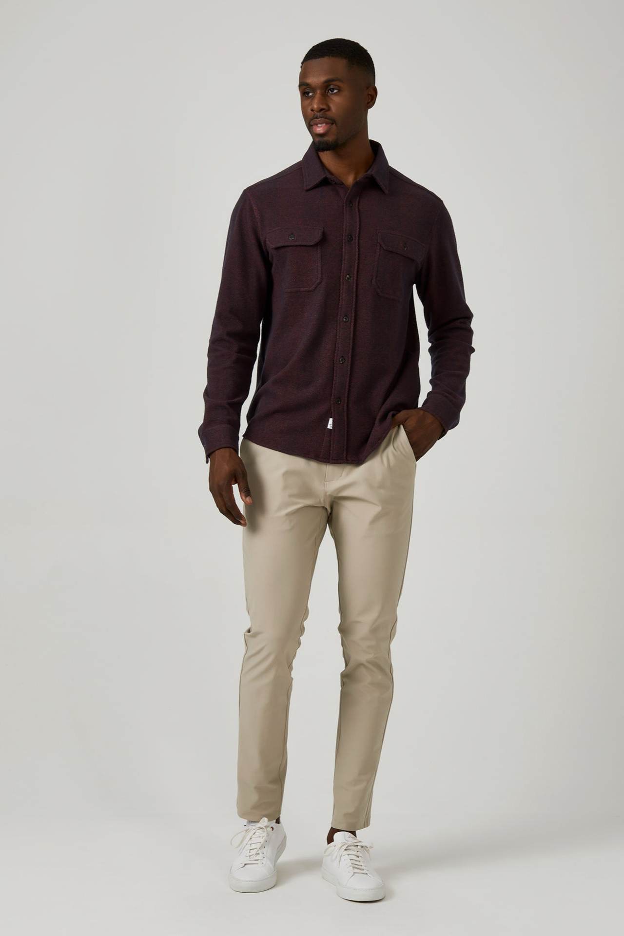 Man wearing a dark brown shirt and beige pants on a white background