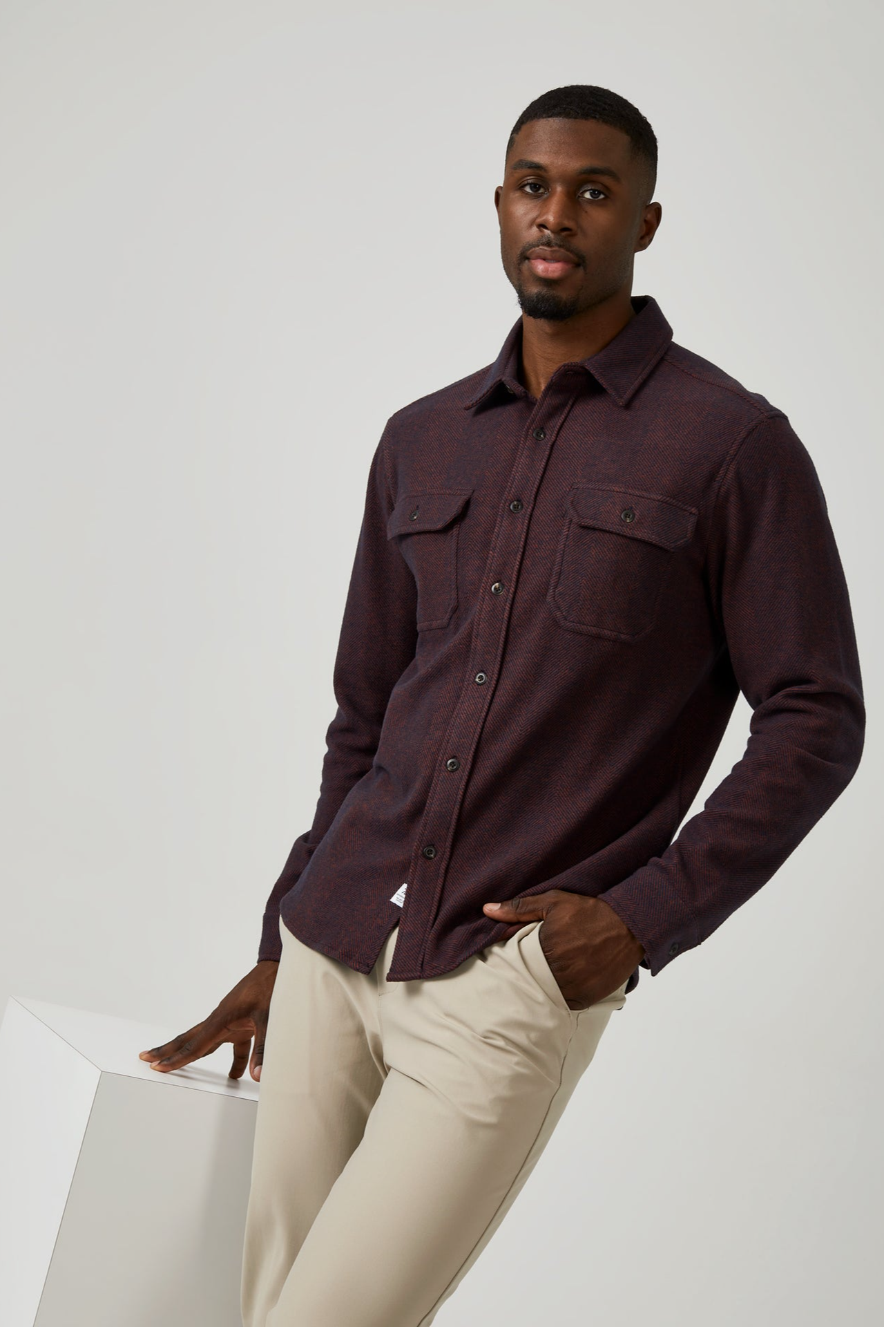 Man wearing a dark brown shirt and beige pants on a white background