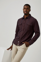 Man wearing a dark brown shirt and beige pants on a white background