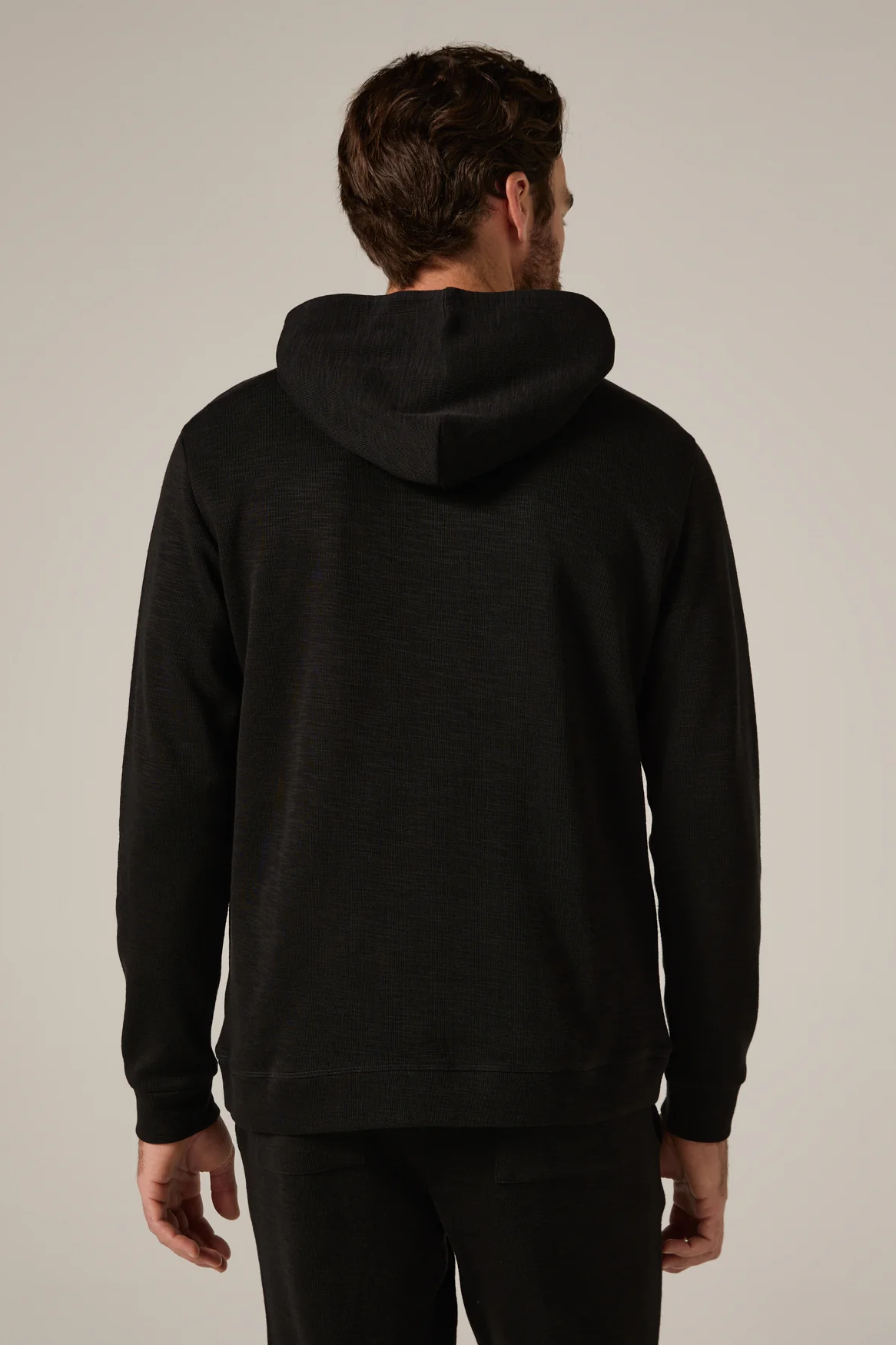 Man wearing a black hoodie from behind on a neutral background