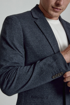 Man wearing a dark gray blazer over a white shirt on a light gray background