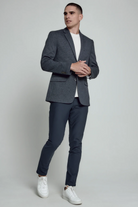 Man wearing a gray blazer, navy pants, and white sneakers on a plain background