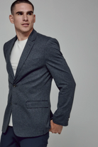 Man wearing a gray blazer over a white shirt on a plain background