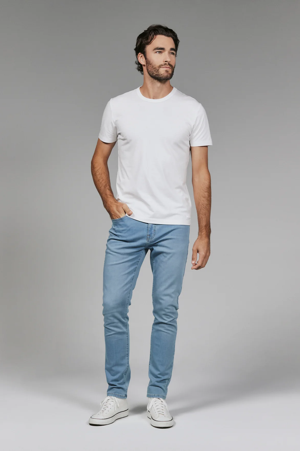 Man wearing a white t-shirt and light blue jeans against a gray background