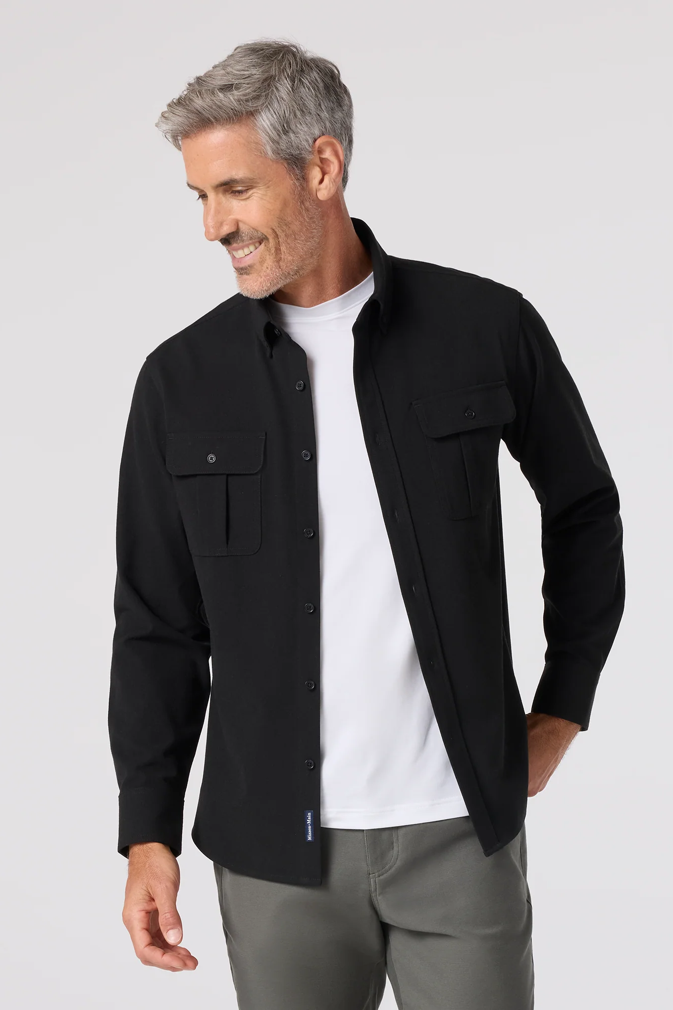 Man wearing a black jacket over a white shirt on a light gray background