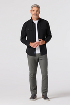 Man wearing a black jacket, white shirt, and gray pants on a white background