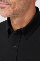 Close-up of a person wearing a black polo shirt with a neutral background