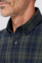 Close-up of a person wearing a green and blue plaid shirt with a neutral background