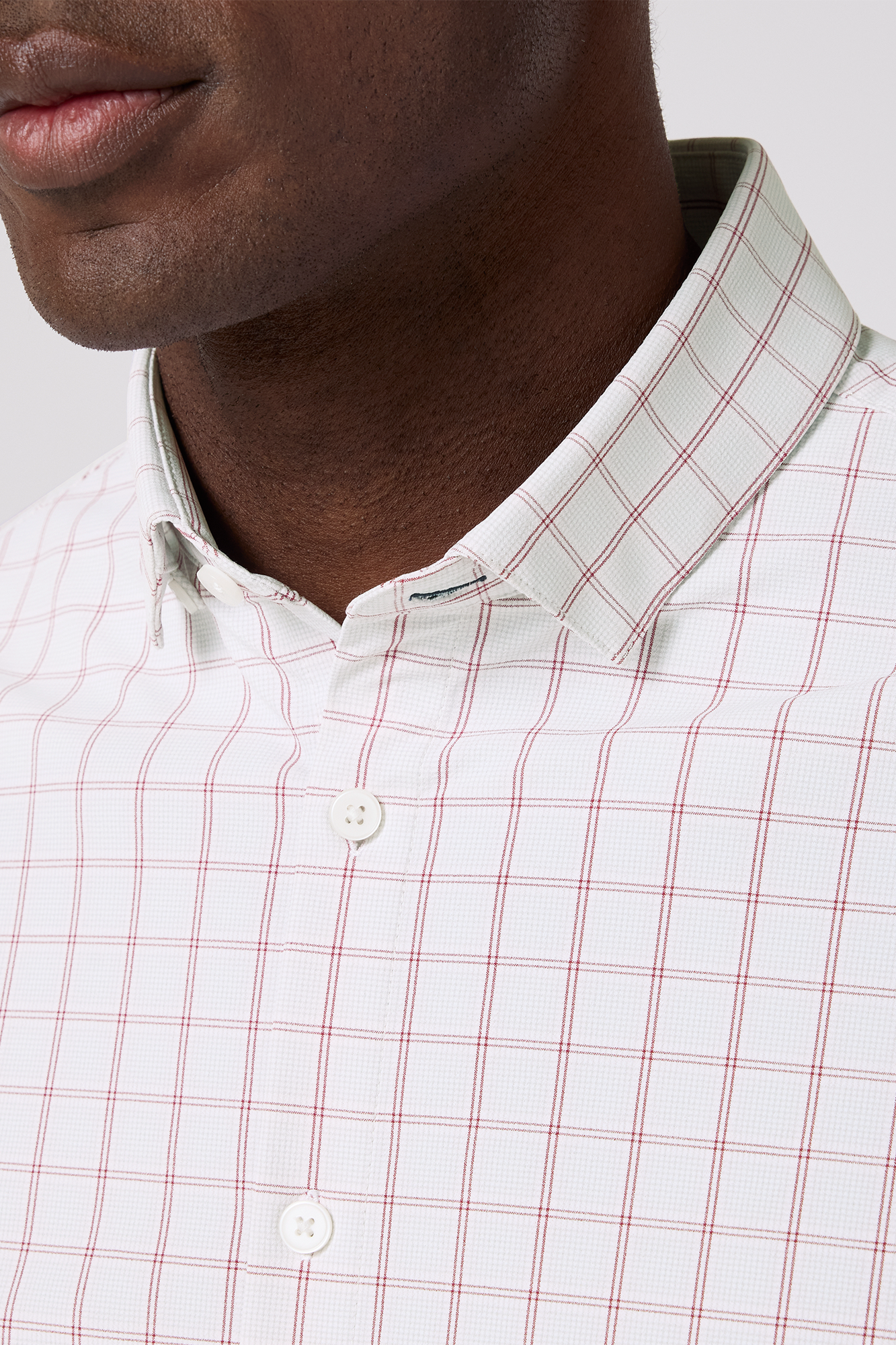 Close-up of a man wearing a white shirt with red plaid pattern on a light gray background