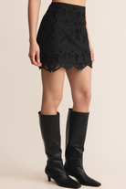 Person wearing a black lace mini skirt and black knee-high boots on a beige background