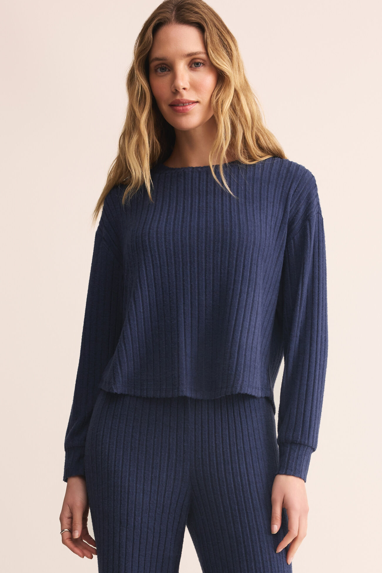 Woman wearing a blue ribbed sweater and pants on a beige background