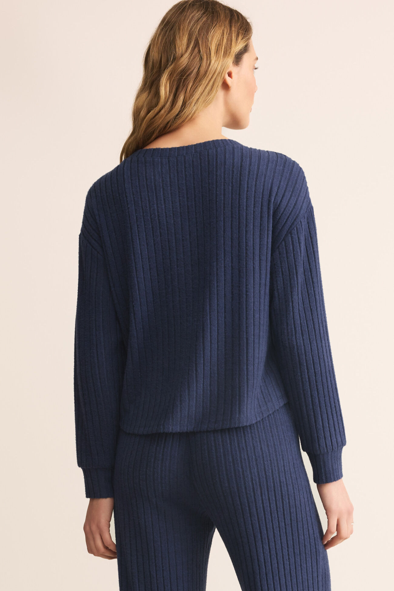 Person wearing a blue ribbed sweater and pants on a beige background