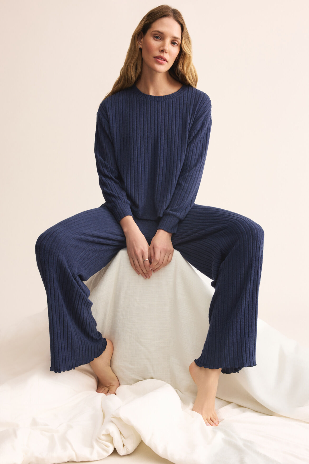 Woman wearing a navy ribbed loungewear set sitting on a white surface.