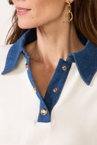 Close-up of a person wearing a white shirt with blue denim collar and gold buttons.