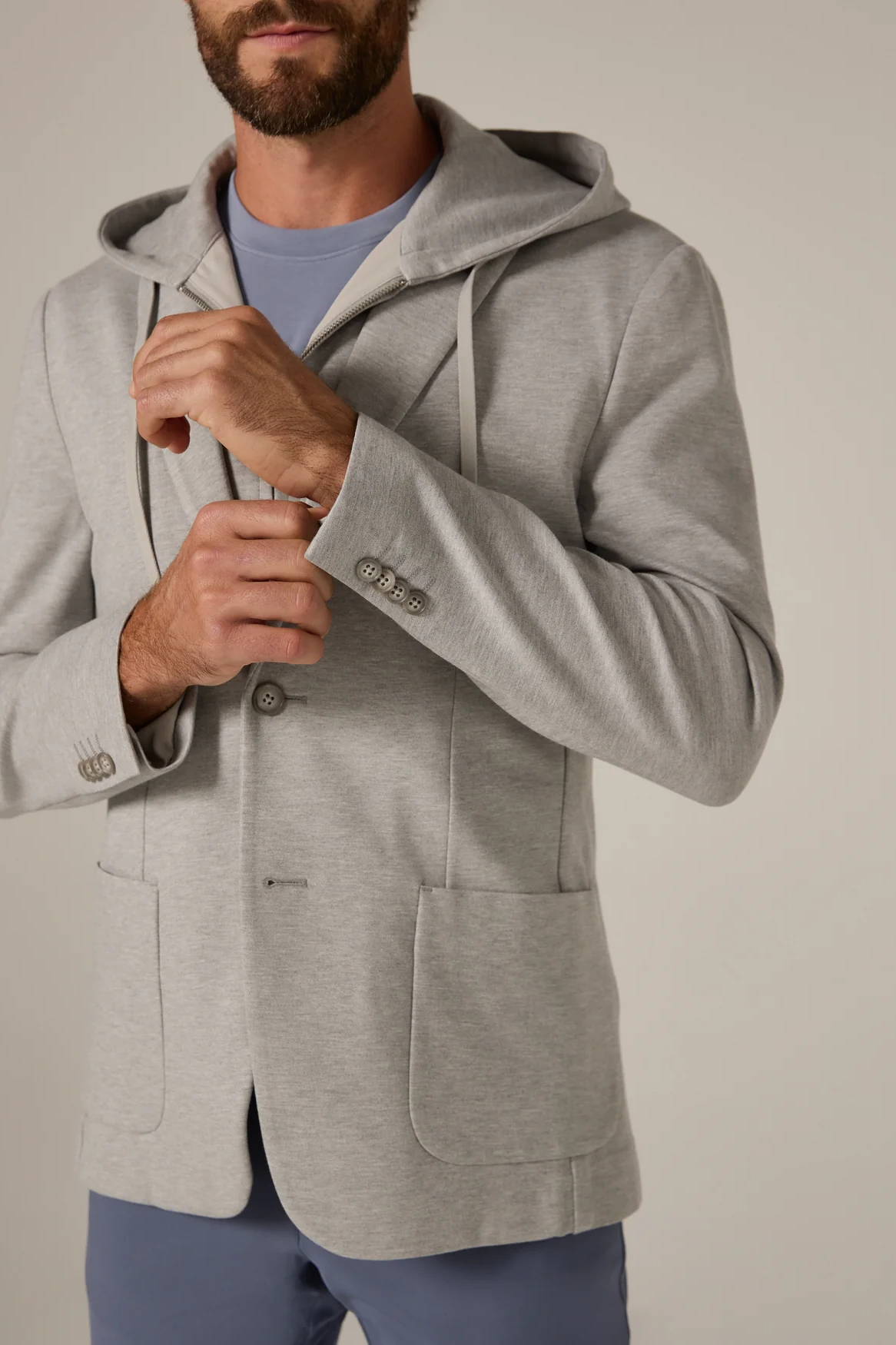 Man wearing a gray hooded jacket against a plain background