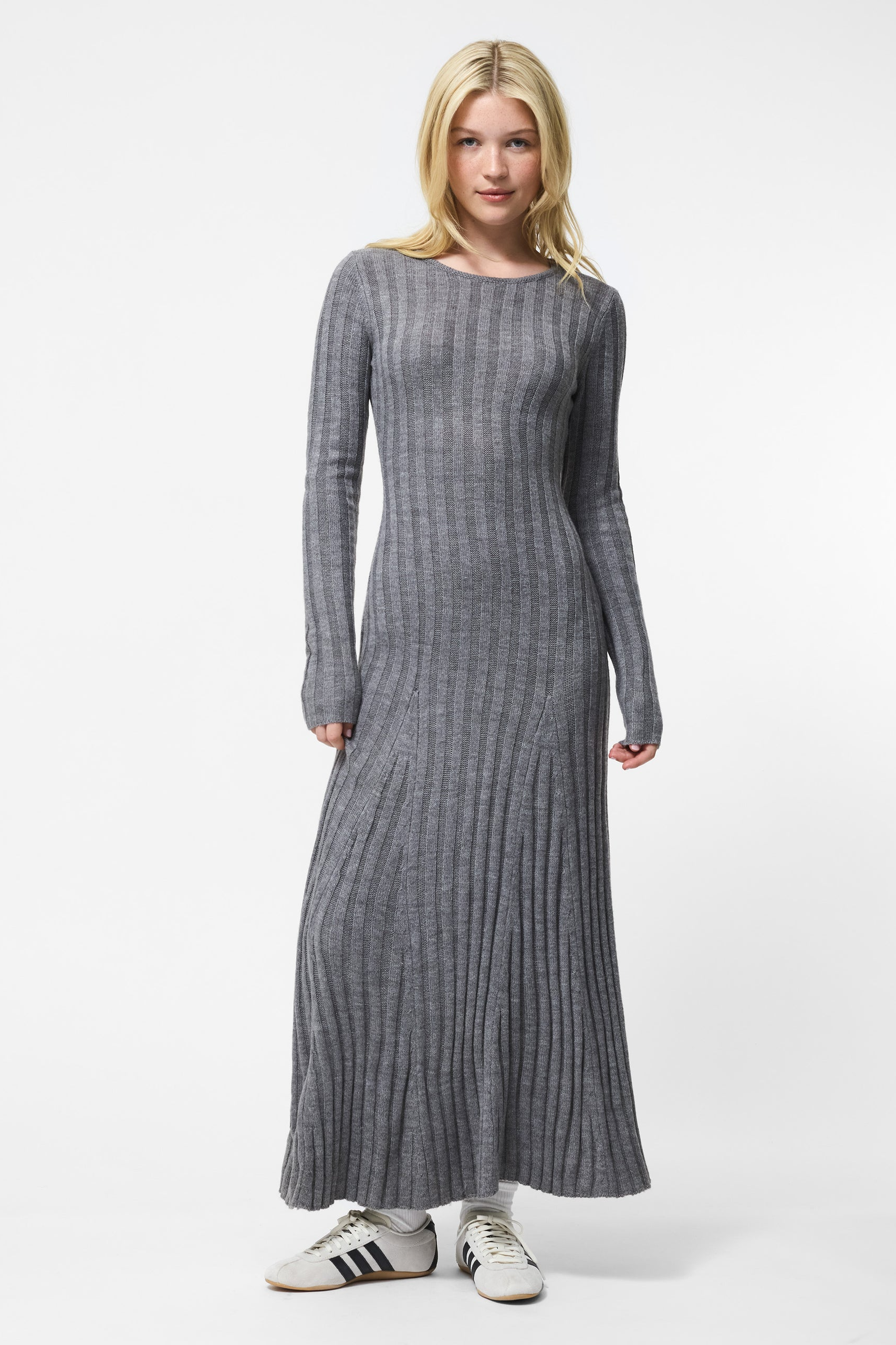 Woman wearing a long gray ribbed dress with white sneakers on a white background