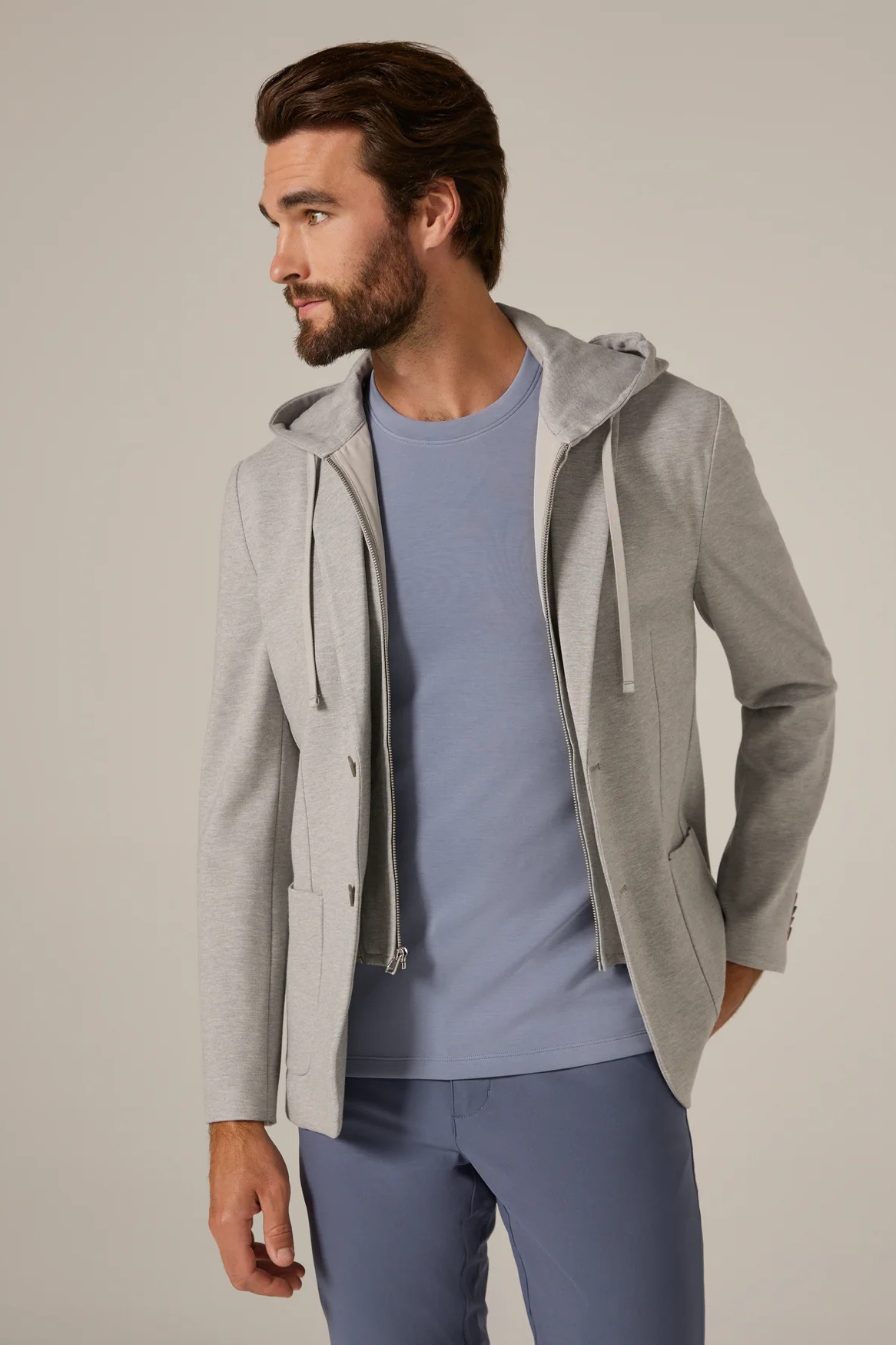 Man wearing a gray hooded jacket over a blue shirt and pants on a plain background