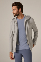 Man wearing a gray hooded jacket over a blue shirt and pants on a plain background