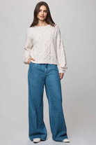 Woman wearing a white cable knit sweater and blue jeans on a gray background