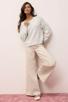 Woman wearing a white patterned cardigan and beige pants on a pink background