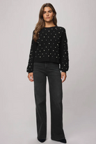 Woman wearing a black sweater with white patterns and black pants on a gray background