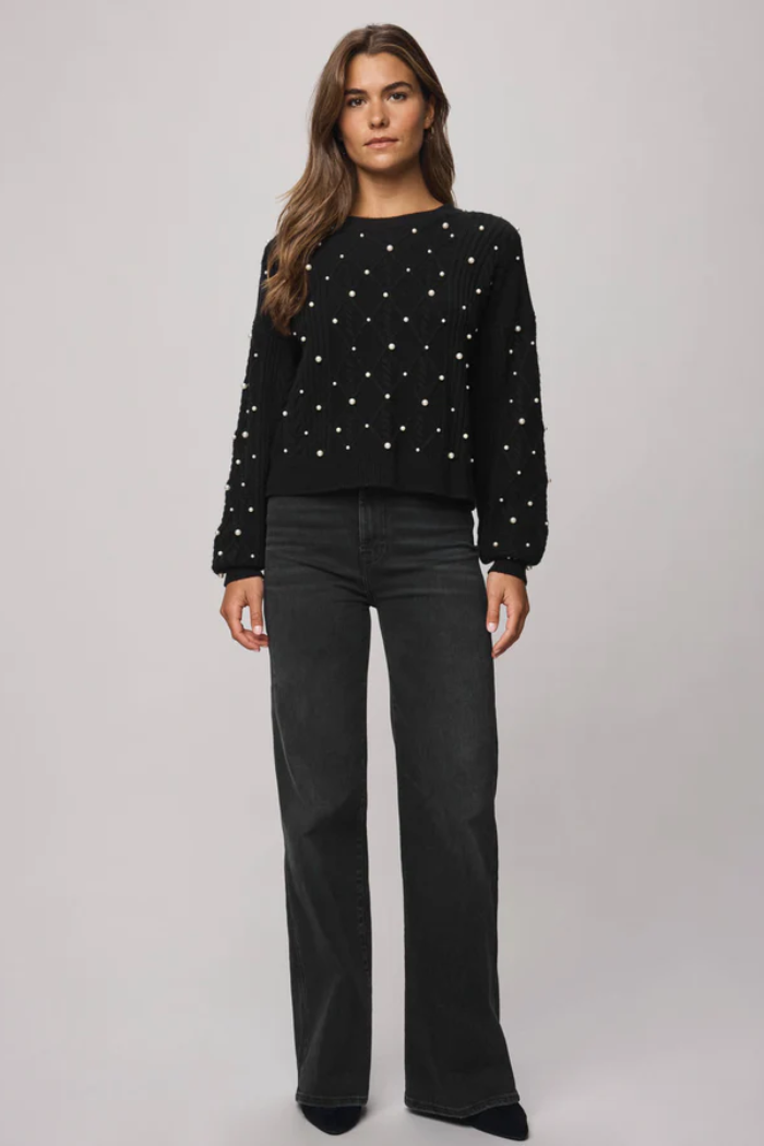 Woman wearing a black sweater with white patterns and black pants on a gray background