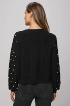 Black sweater with pearl embellishments on a gray background