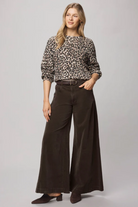 Woman wearing a leopard print top and brown wide-leg pants on a gray background