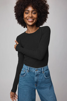 Woman wearing a black long-sleeve top and blue jeans against a gray background