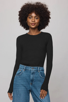 Woman wearing a black long-sleeve top and blue jeans against a plain background