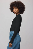 Woman wearing a black long-sleeve top and blue jeans against a gray background