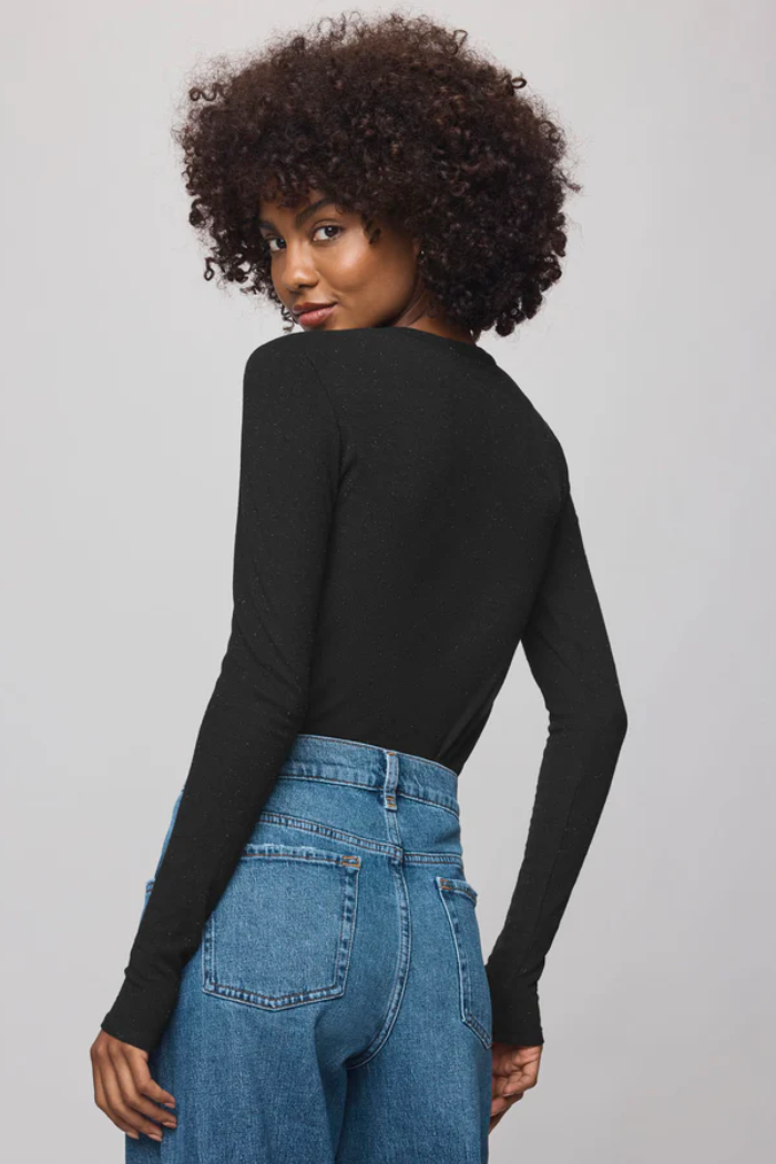 Woman wearing a black long-sleeve top and blue jeans on a gray background