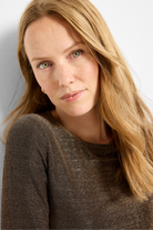 Woman with long blonde hair wearing a brown textured top against a plain background