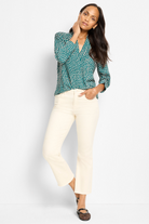 Woman wearing a green patterned blouse and white pants against a white background