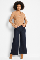 Woman wearing a patterned blouse and dark blue jeans on a white background