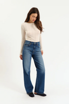 Woman wearing blue jeans and a beige top on a white background
