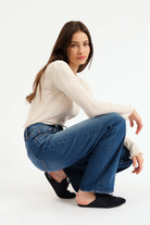 Woman wearing a white sweater and blue jeans on a white background