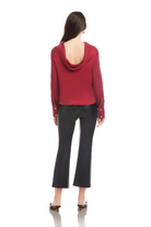 Person wearing a red hoodie with open back and black pants on a white background