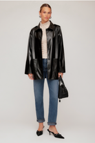 Woman wearing a black leather jacket, blue jeans, and a beige sweater on a white background