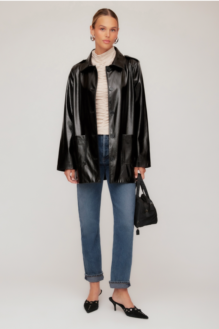 Woman wearing a black leather jacket, blue jeans, and a beige sweater on a white background