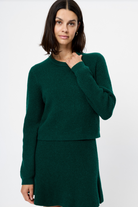 Woman wearing a green sweater and skirt set on a white background