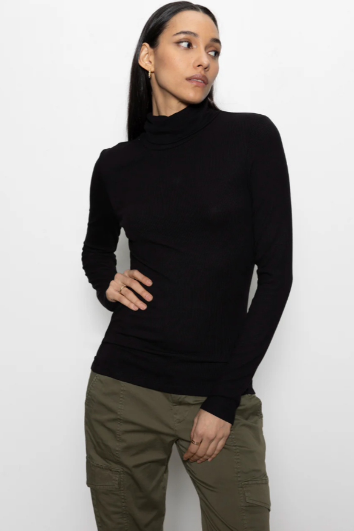 Person wearing a black turtleneck and green pants on a white background